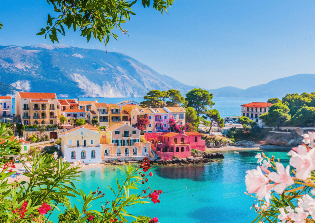Widok na kolorowe domy w nadmorskiej miejscowości Assos na wyspie Kefalonia z turkusową wodą w tle.