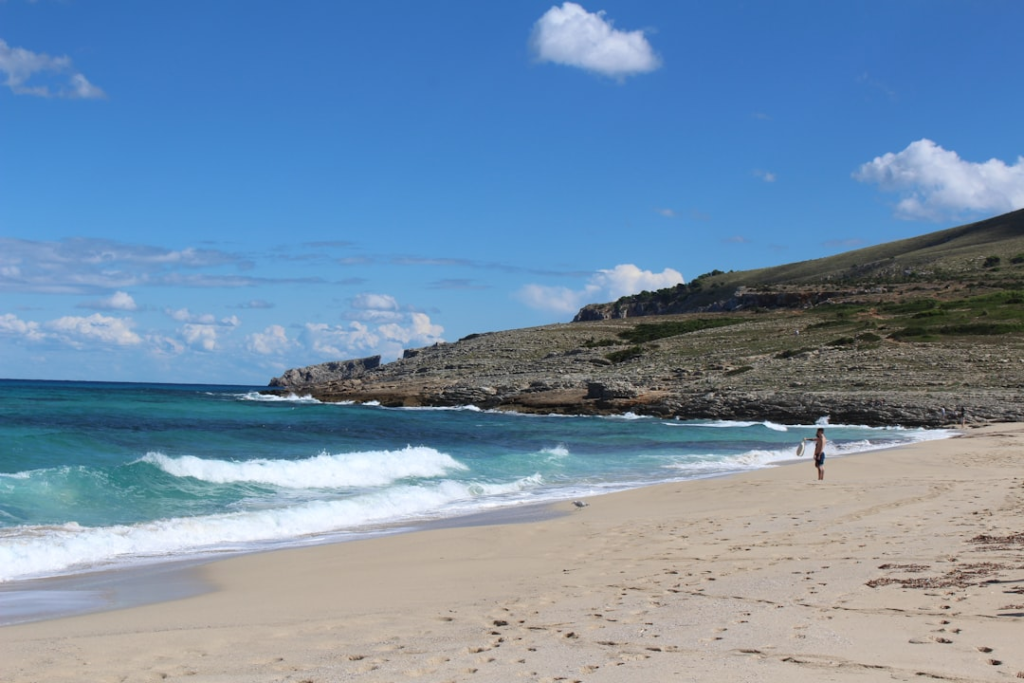 Panorama plaży Cala Mesquida z jasnym piaskiem, lazurowym morzem i wydmami.