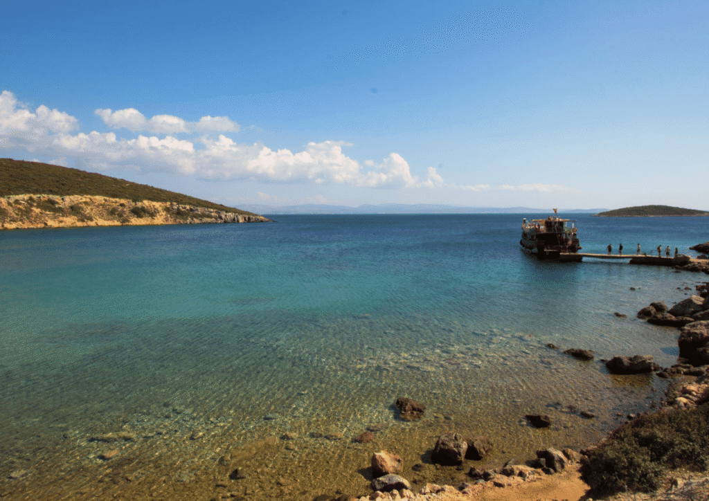 Plaża i spokojne wody zatoki w Çeşme z łodzią na horyzoncie, Turcja Egejska