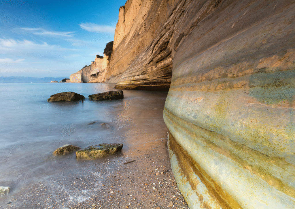 Pionowe, warstwowe klify nad spokojnym morzem o zachodzie słońca – Loggas Beach w pobliżu Sidari, Korfu