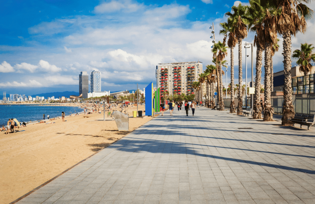 Plaża Barceloneta z promenadą, palmami i turystami spacerującymi wzdłuż wybrzeża, Barcelona