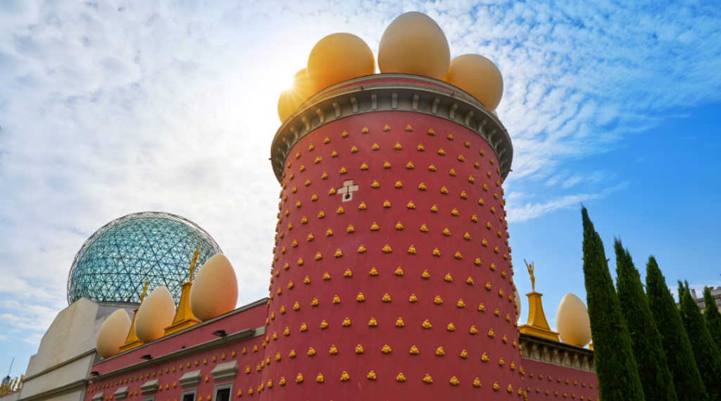 Budynek teatru–muzeum Salvadora Dalí w Figueres – charakterystyczna czerwona fasada ozdobiona ogromnymi złotymi jajami i przylegająca szklana kopuła.