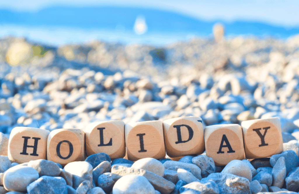 Drewniane kostki z napisem "HOLIDAY" na kamienistej plaży — symbol beztroskich wakacji w maju