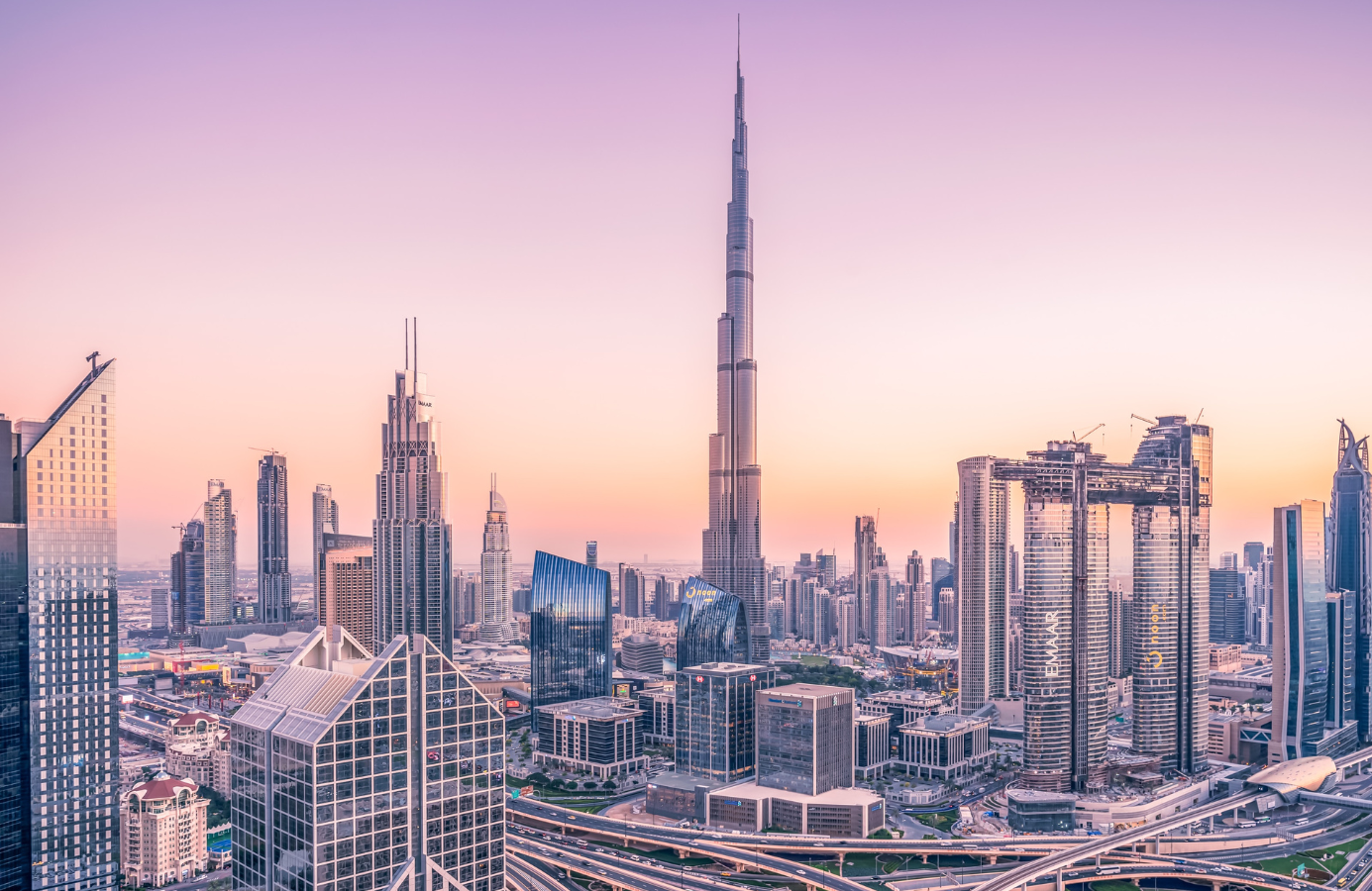 Panorama centrum Dubaju o zachodzie słońca z dominującym wieżowcem Burdż Chalifa otoczonym nowoczesnymi drapaczami chmur i drogami szybkiego ruchu