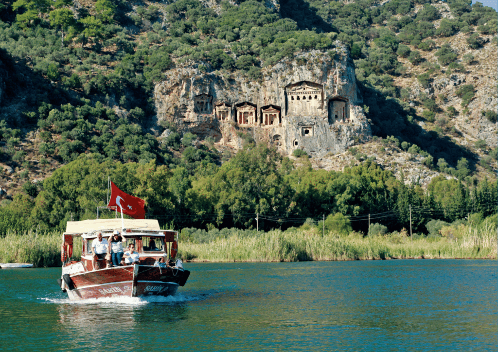Łódź turystyczna płynąca rzeką Dalyan z widokiem na skalne grobowce licyjskie, Turcja Egejska
