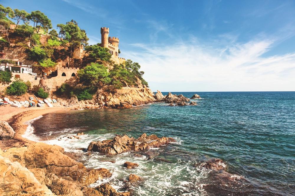 Widok na skaliste wybrzeże Costa Brava z zamkiem nad zatoką i turkusowym morzem – idealne miejsce na wakacje w Hiszpanii
