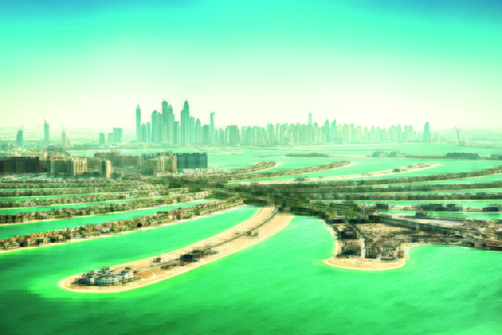 Widok z lotu ptaka na sztuczną wyspę Palm Jumeirah z drapaczami chmur Dubaju w tle, otoczoną turkusową wodą Zatoki Perskiej