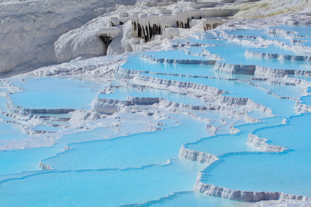 Białe tarasy mineralne Pamukkale wypełnione turkusową wodą.