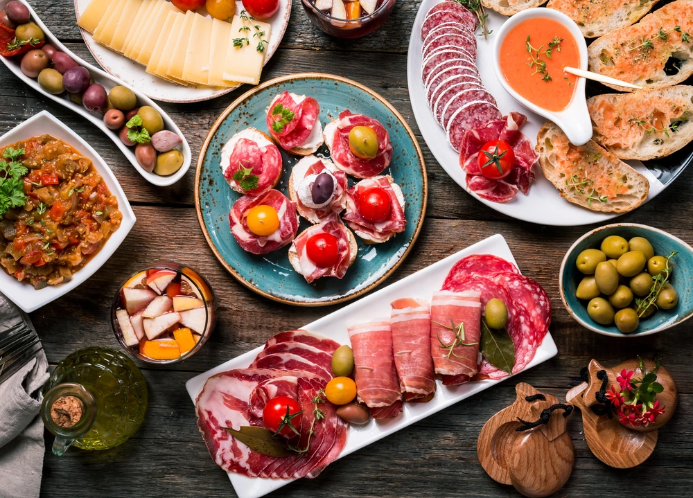 Hiszpańskie tapas – talerze z oliwkami, wędlinami, serem, grzankami i sangrią na drewnianym stole
