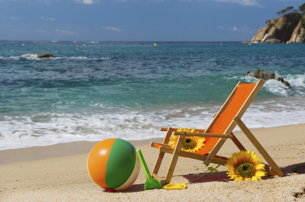 Leżak plażowy z pomarańczowym oparciem, kolorowa piłka plażowa i słoneczniki na piaszczystej plaży nad lazurowym morzem