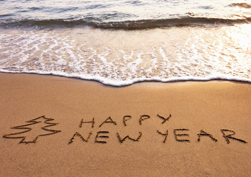 Napis „Happy New Year” na piasku przy brzegu morza, symbolizujący sylwestra za granicą