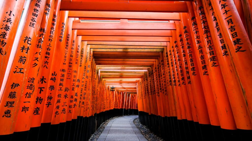 Mnich w tradycyjnym stroju przechodzący przez czerwone bramy torii w świątyni Fushimi Inari