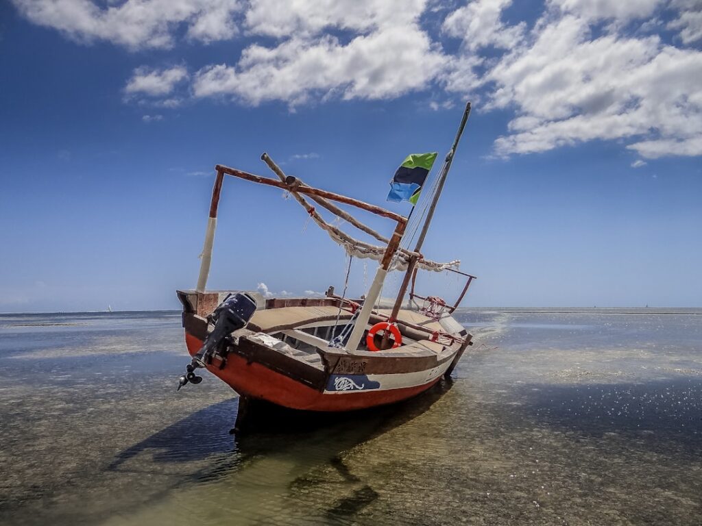 Zanzibar – żółta łódź na białej plaży z Masajem