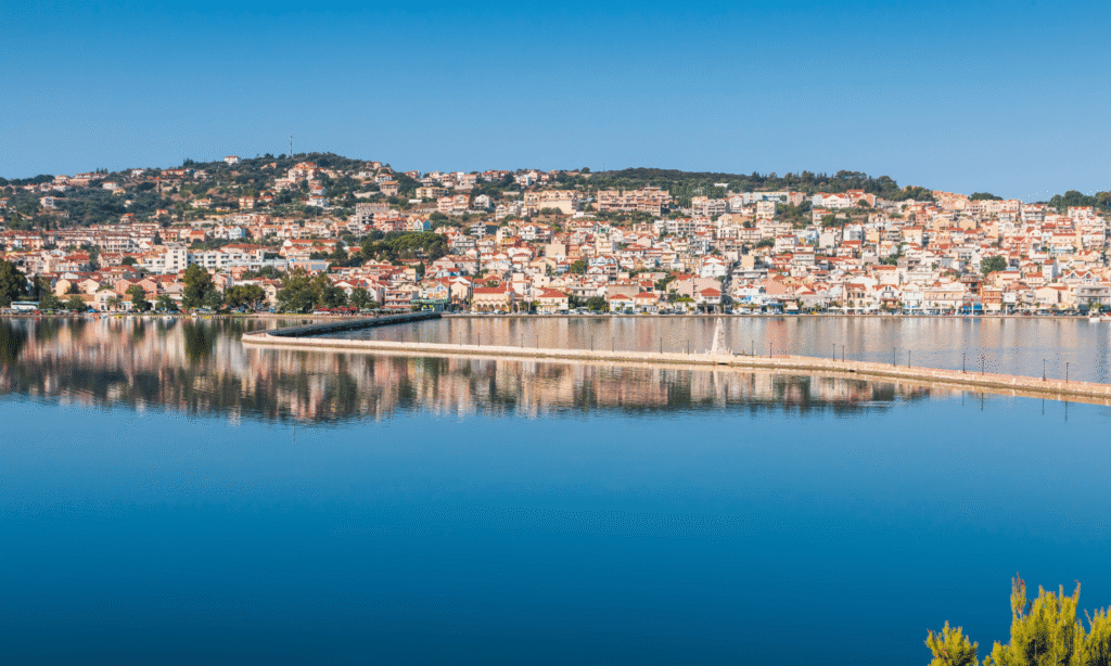 Panorama miasta Argostoli na Kefalonii z widokiem na promenadę i odbijające się w wodzie kolorowe budynki.