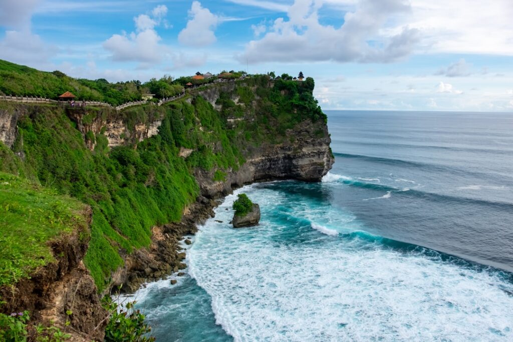 Małpa siedząca na barierce z widokiem na klify i ocean przy świątyni Uluwatu na Bali