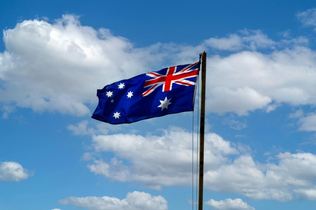 Osoba trzymająca flagę Australii na tle zachodu słońca nad oceanem