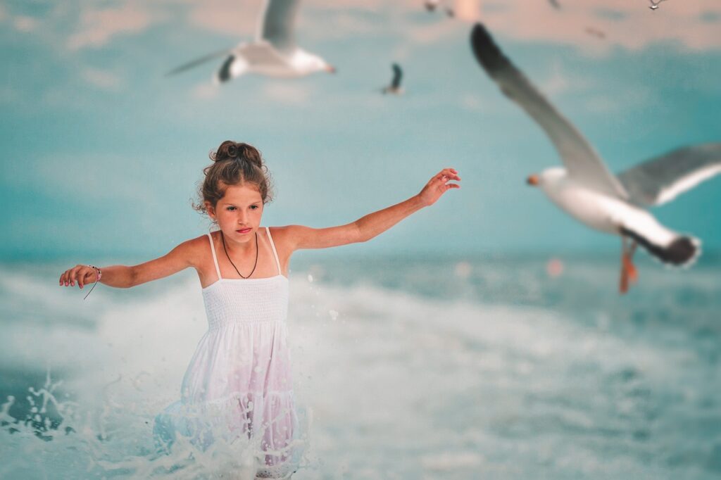 Uśmiechnięty chłopiec w kapeluszu i okularach przeciwsłonecznych leży na ręczniku w pasy podczas wakacji z dzieckiem