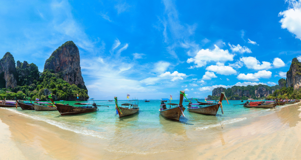 Railay Beach w Tajlandii – tropikalna plaża z tradycyjnymi łodziami na tle wapiennych klifów.