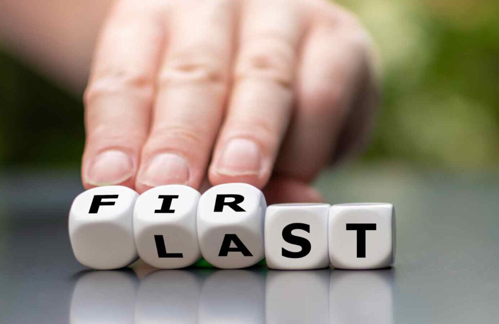 Ręka przekręcająca kostki z napisem "LAST" i "FIRST" – wybór między ofertą Last Minute a First Minute