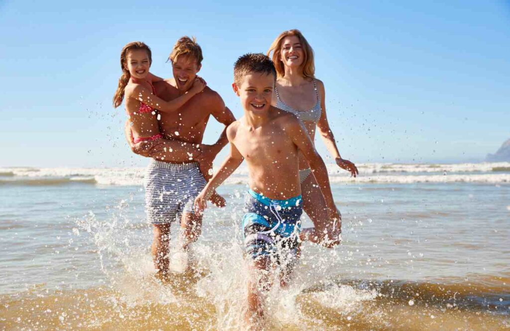 Rodzina z dwójką dzieci biegnąca po plaży – beztroskie wakacje z dziećmi nad morzem