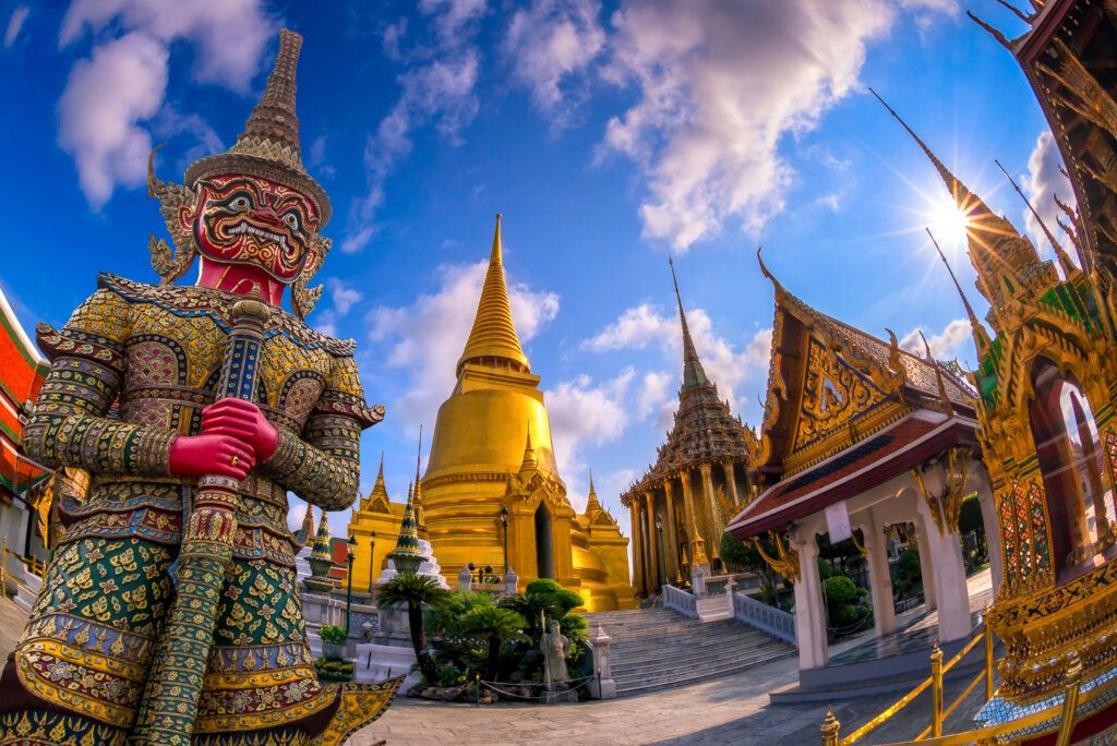 Złota świątynia Wat Phra Kaew w Bangkoku z posągiem strażnika yaksha i błękitnym niebem w tle