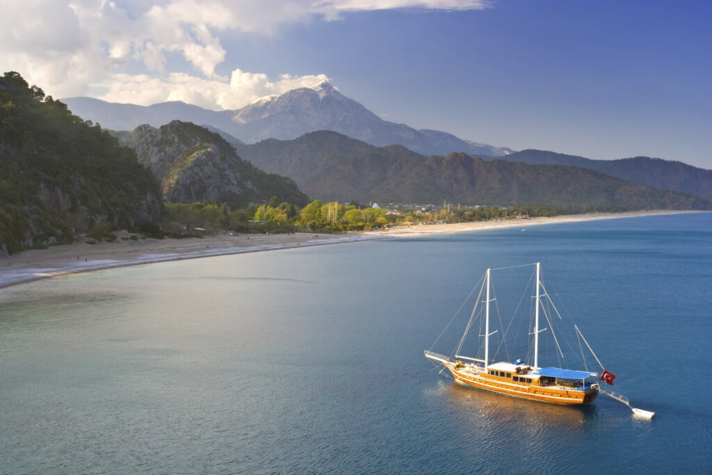 Plaża w Kemer w Turcji z górskim krajobrazem w tle i tradycyjnym tureckim statkiem żaglowym na turkusowym morzu
