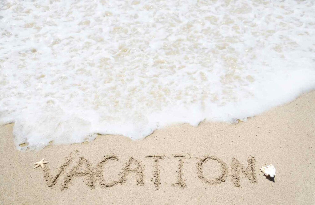Słowo „VACATION” napisane na piasku tuż przy linii fal – wakacyjna atmosfera na plaży