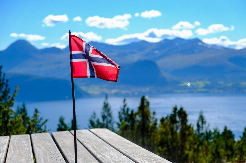 Flaga Norwegii powiewająca nad fiordem, góry i woda podczas rejsu