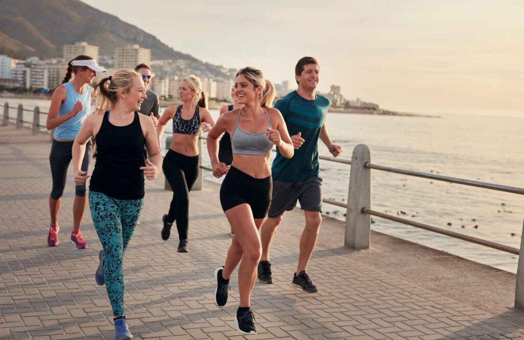 Grupa osób biegnąca wzdłuż nadmorskiej promenady – wakacyjny running club