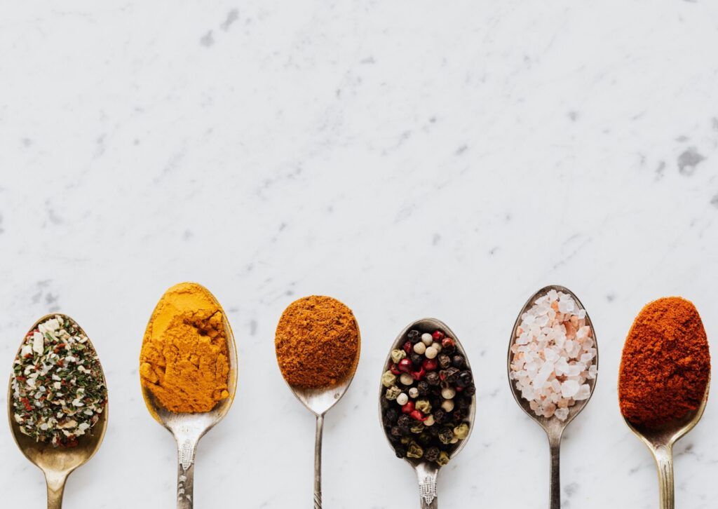 Przyprawy arabskie na metalowych łyżkach – kurkuma, papryka, pieprz i sól himalajska na jasnym tle