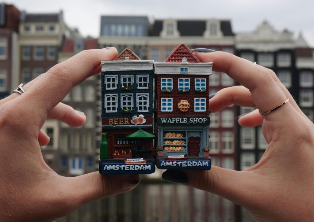 Magnesy z kamienicami Amsterdamu trzymane w dłoniach na tle zabytkowej zabudowy miasta