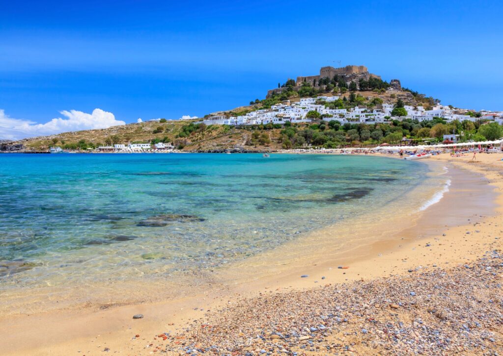 Majówka na Rodos – plaża i białe domy Lindos z akropolem na wzgórzu