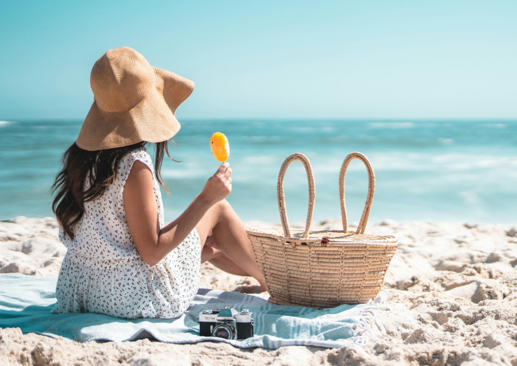 Kobieta siedząca na plaży z kapeluszem i koszem piknikowym nad morzem w Hiszpanii