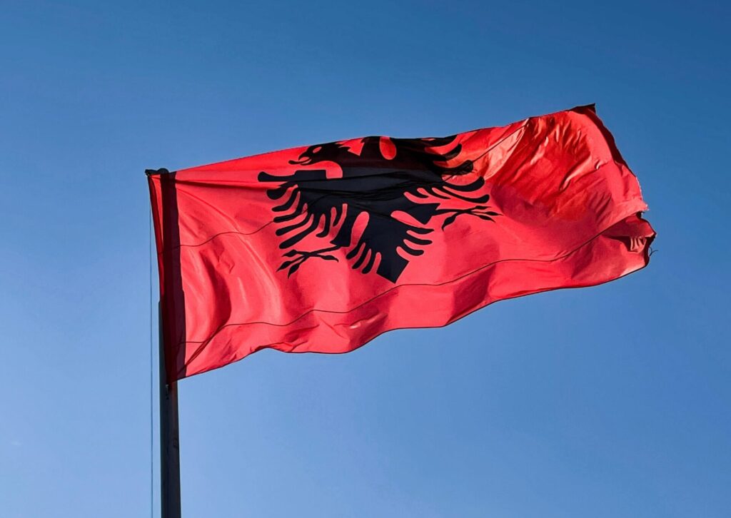Czerwona flaga Albanii z czarnym dwugłowym orłem powiewająca na maszcie na tle błękitnego nieba