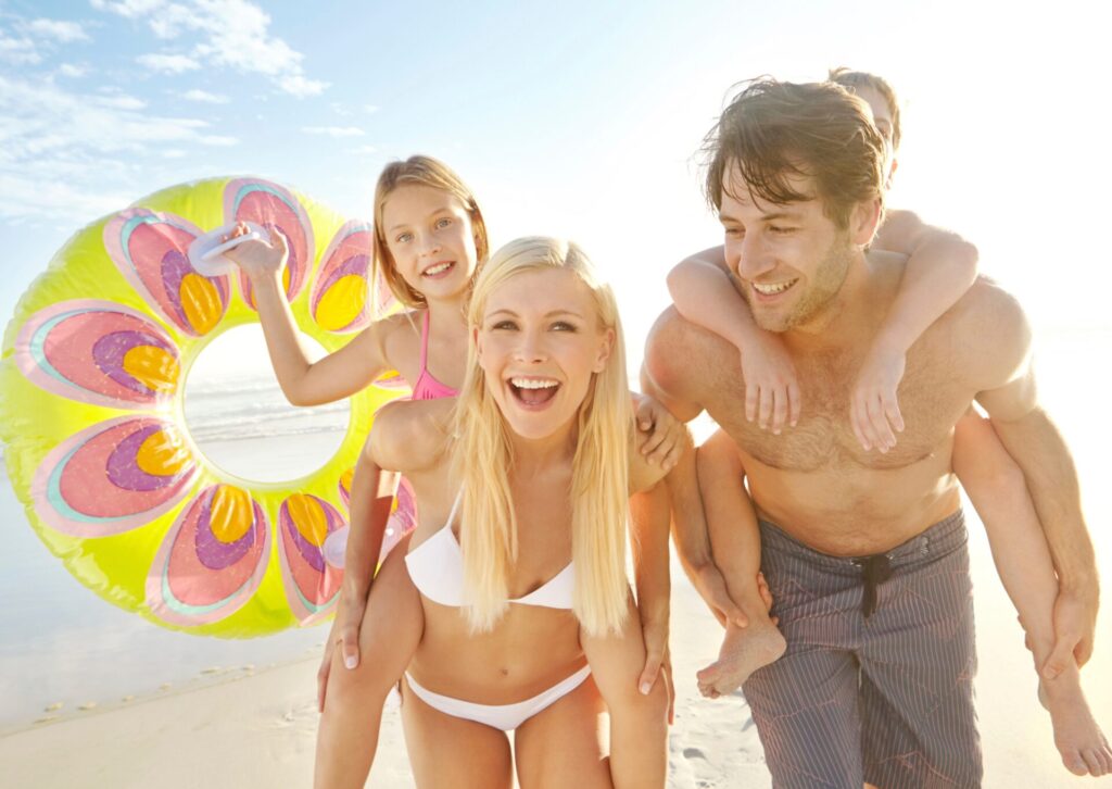 Szczęśliwa, uśmiechnięta rodzina z dwójką dzieci bawi się na słonecznej plaży podczas wakacji All Inclusive